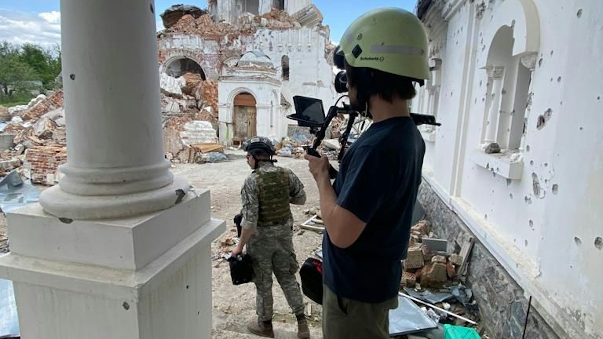 Ein Mann mit Kamera steht vor einer zerstörten Kirche.