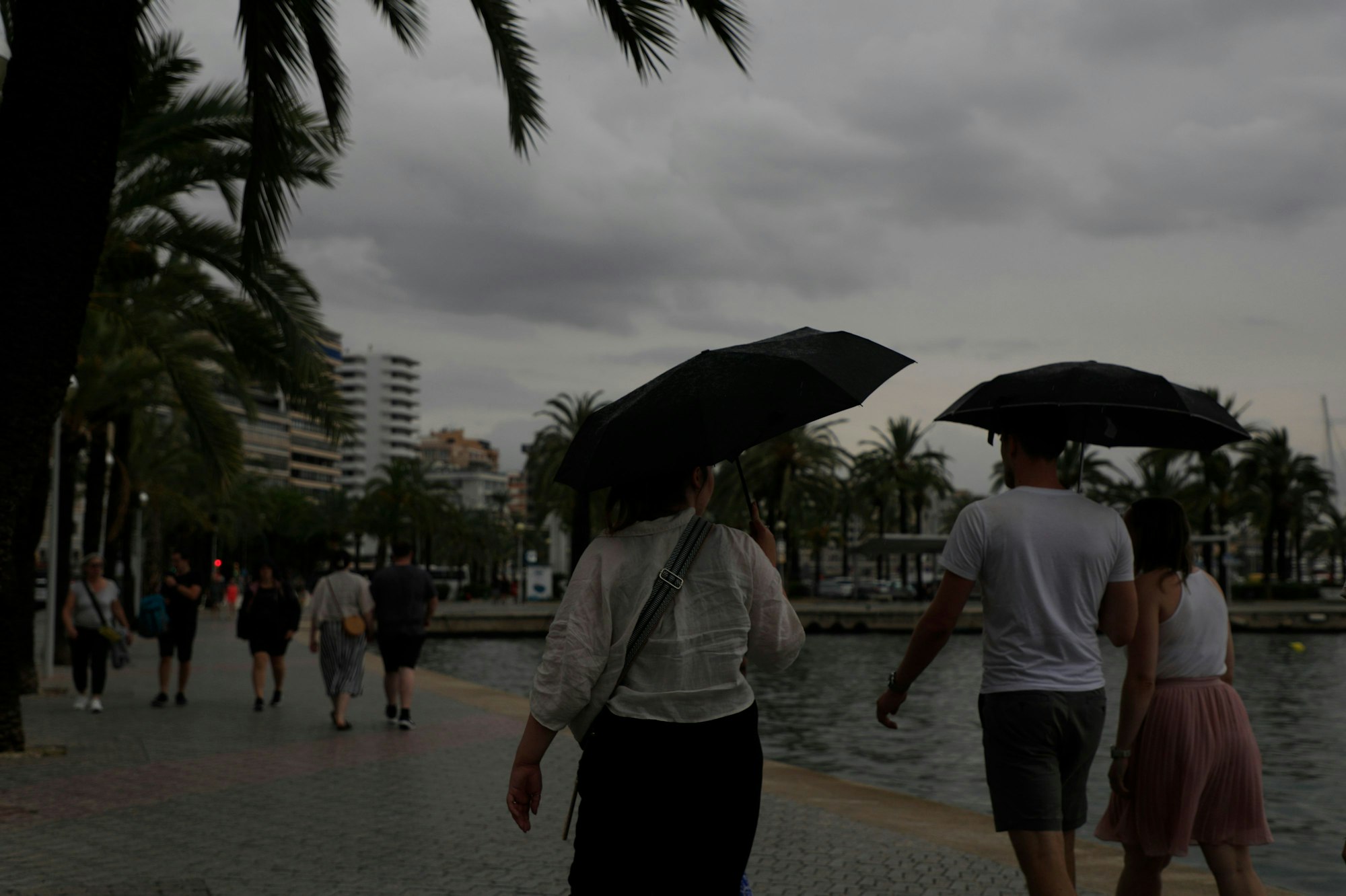 Mit Schirmen sind Spaziergänger an der Strandpromenade unterwegs.