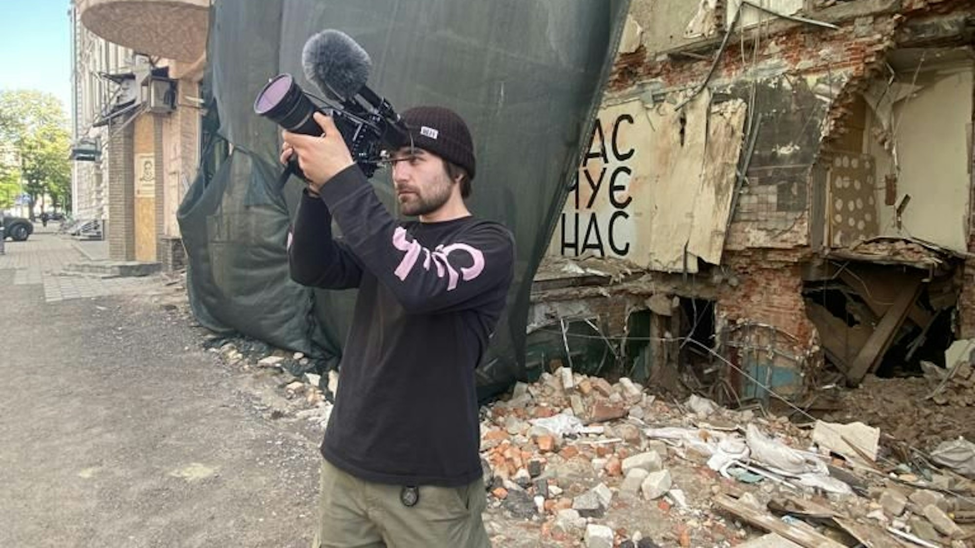 Das Foto zeigt den Filmemacher vor zerstörten Gebäude in der Ukraine.
