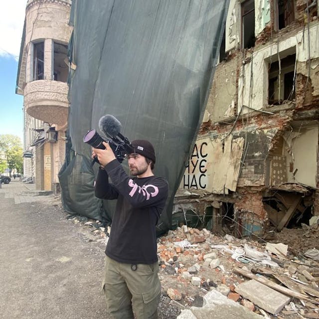 Das Foto zeigt den Filmemacher vor zerstörten Gebäude in der Ukraine.&nbsp;