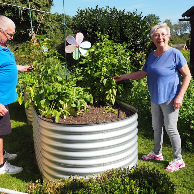Ein Mann und eine Frau stehen in einem Garten links und rechts von einem ovalen Hochbeet mit Paprikapflanzen.&nbsp;
