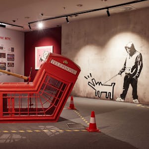 Mitarbeiter gehen in der Ausstellung "The Mystery of Banksy - A Genius Mind". Im Vordergrund ist die Installation "Death Of Telephone Booth" zu sehen.
