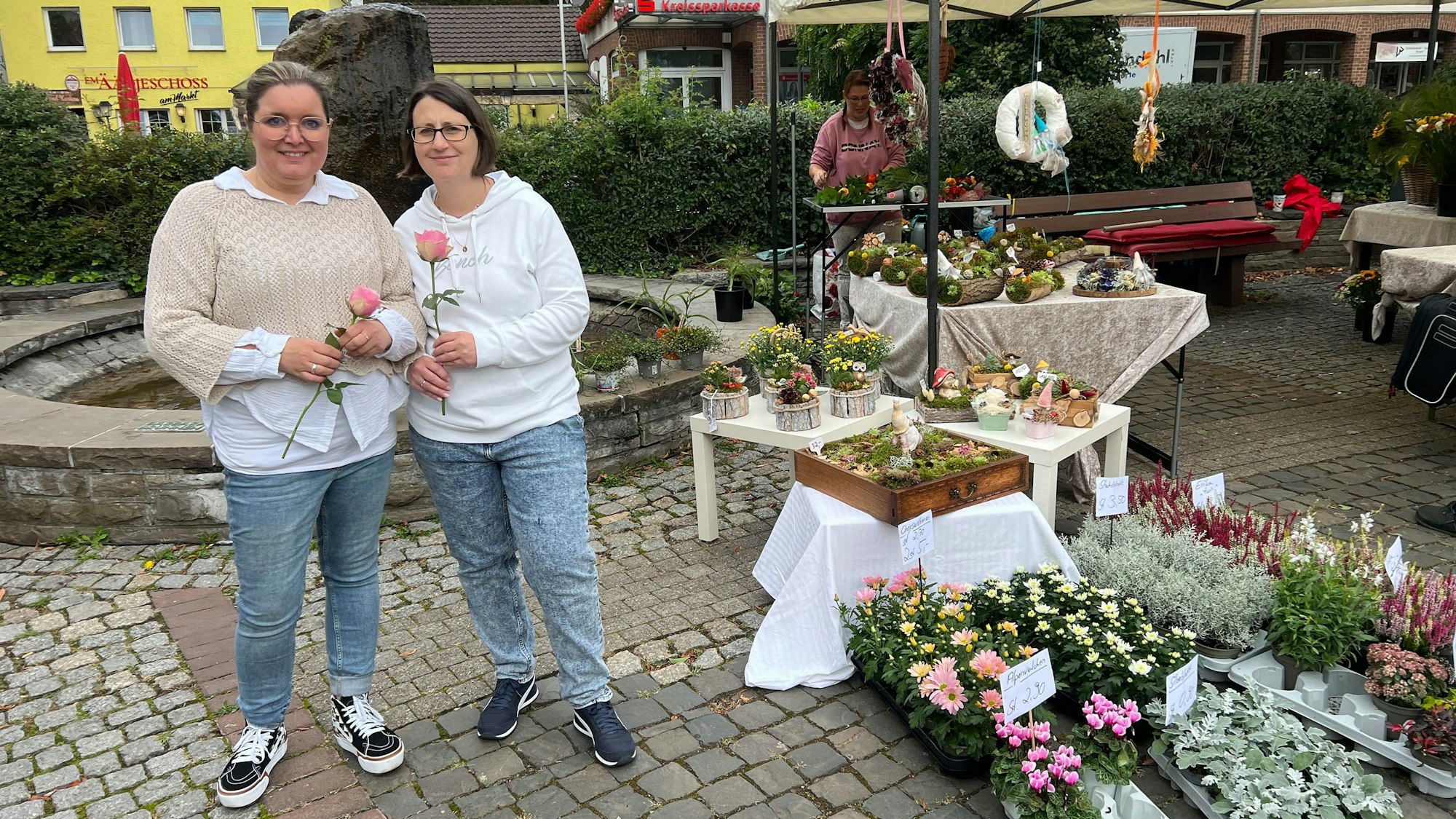 Zwei Frauen neben einem Marktstand mit Blumen.