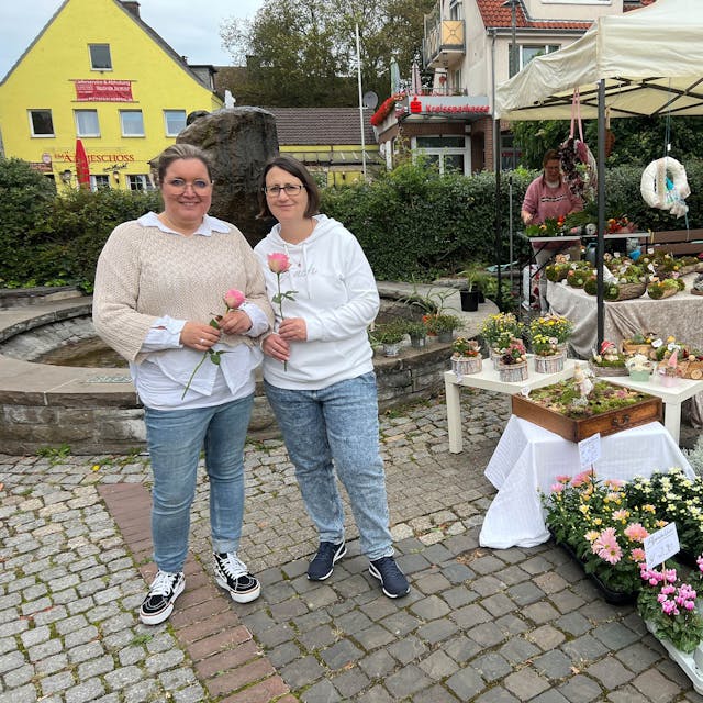 Zwei Frauen neben einem Marktstand mit Blumen.