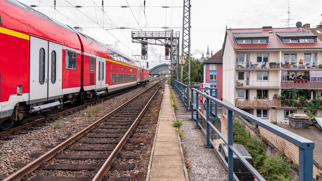 Ein Regionalexpress der Deutschen Bahn fährt über die Gleise an einem Wohngebiet in Köln vorbei.