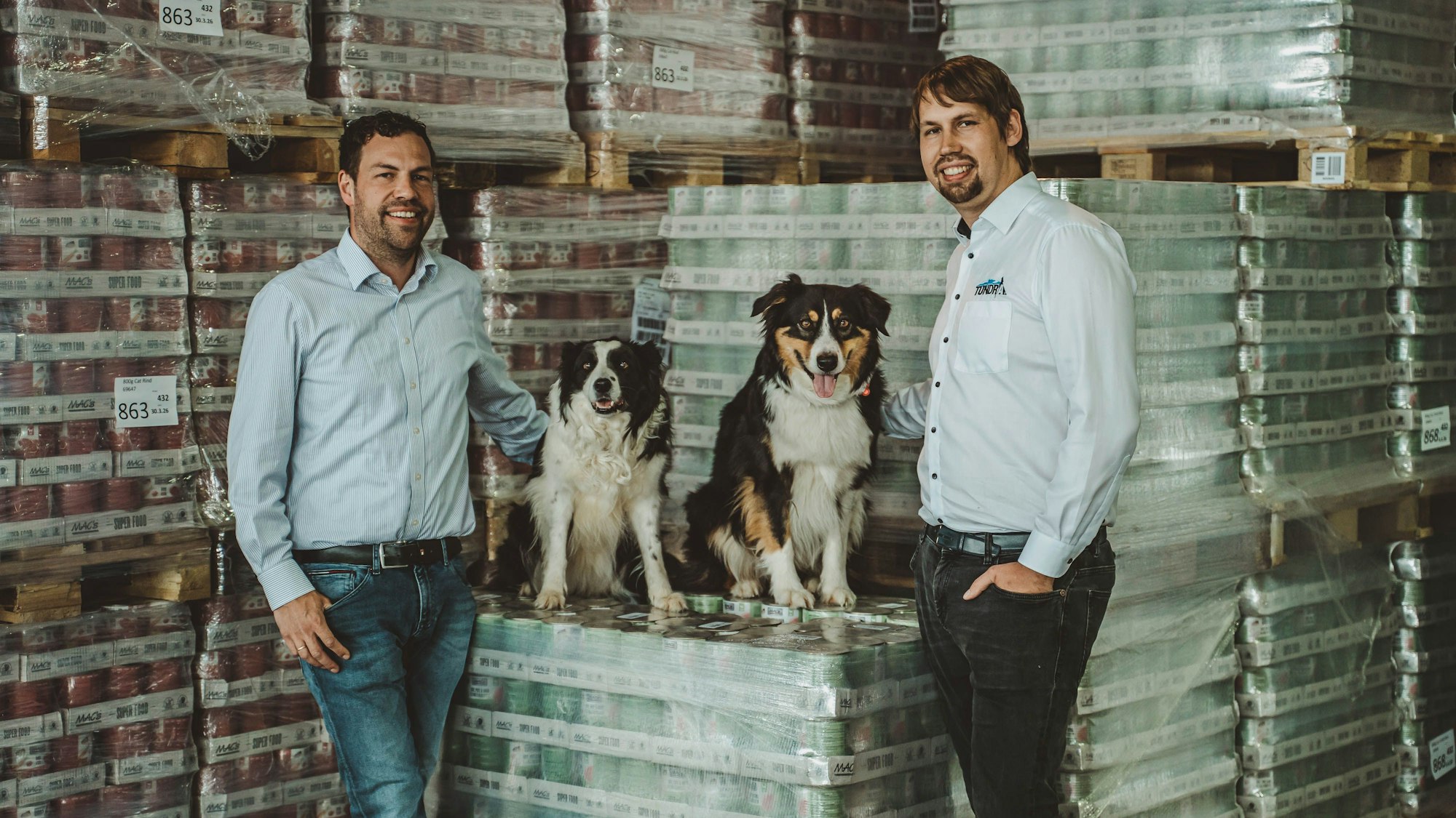 Markus (r.) und Michael Koller sind die Geschäftsführer der Kaller Firma Pro Pet. Auf dem Bild sind sie mit ihren Hunden im Lager mit den auf Paletten gepackten Tiernahrungs-Dosen zu sehen.