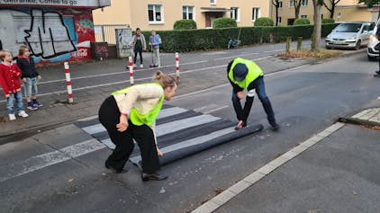 Helfer rollen einen Zebrastreifen-Teppich auf der Straße aus.