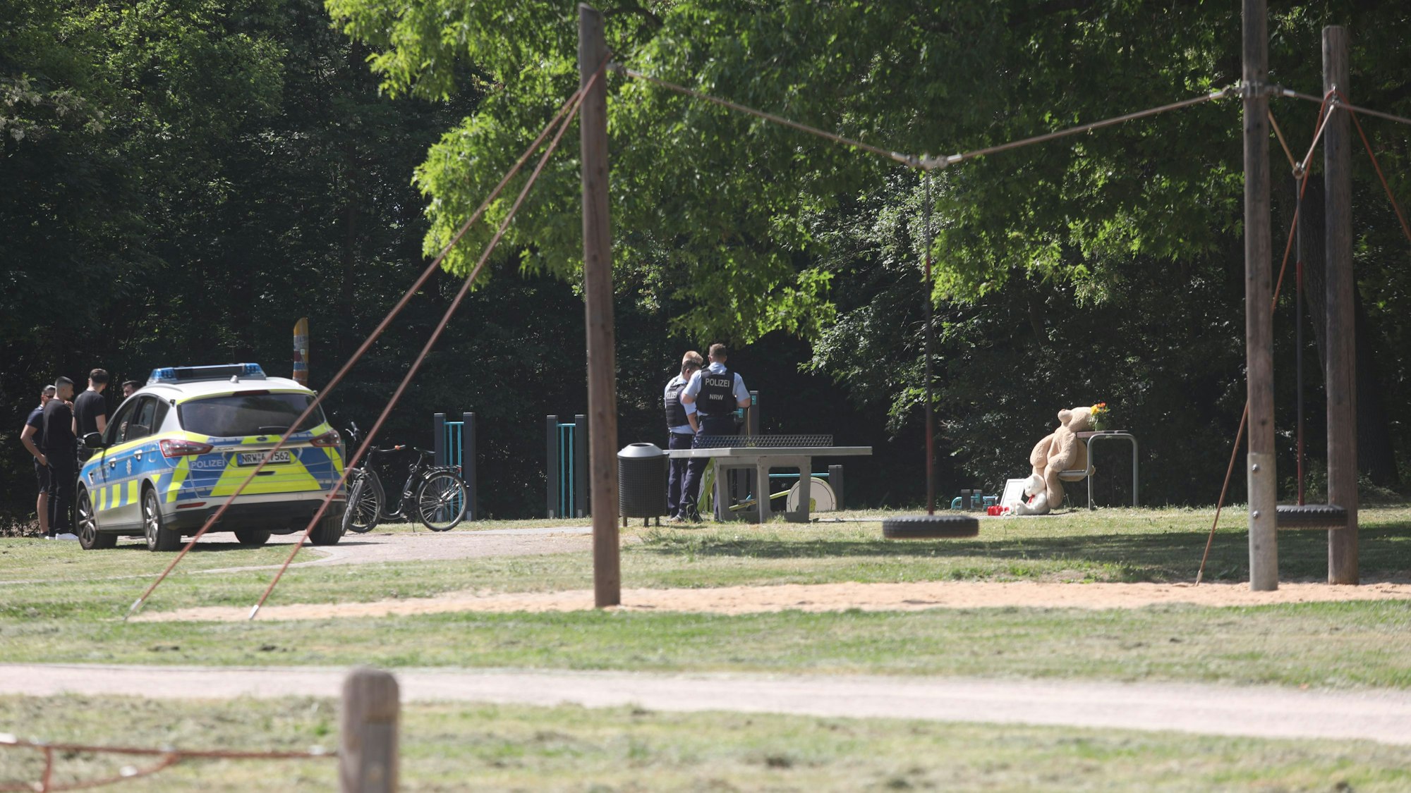 Ein Streifenwagen steht auf einem Spielplatz, auf dem sich auch mehrere Einsatzkräfte der Polizei befinden.