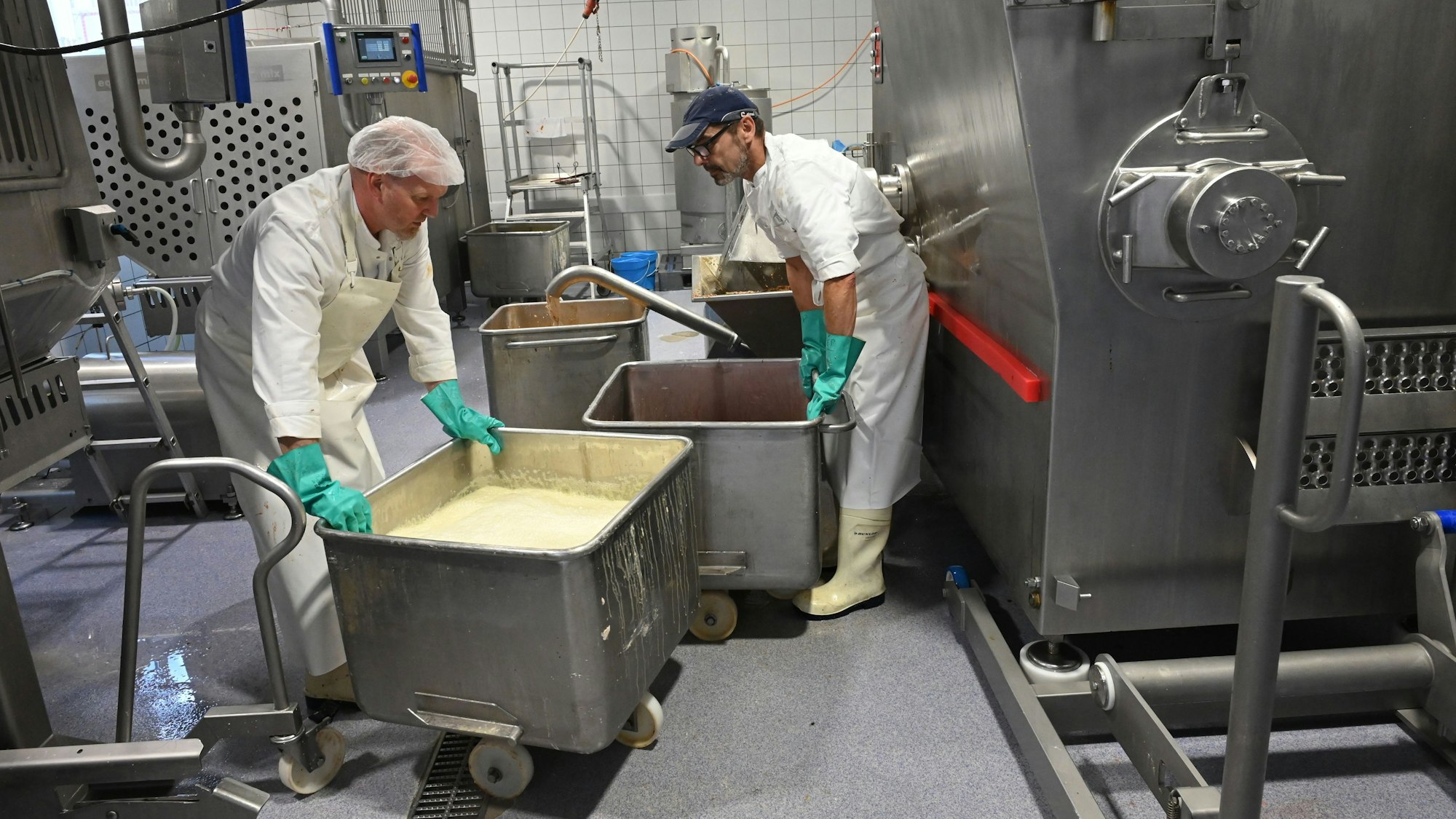 Zwei Männer stehen in einem Raum voller Maschinen an zwei großen Bottichen. Darin wird die Mischung für Tierfutter zubereitet.