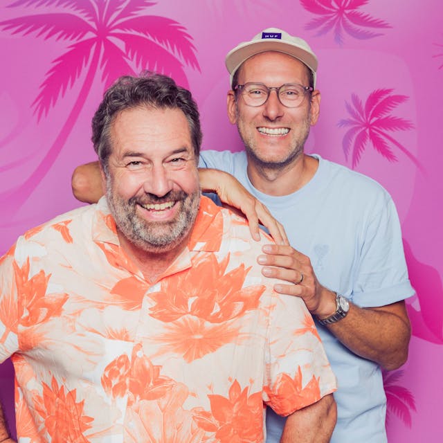 Autor Andreas Hutzler (links) und Kommentator Simon Beeck vor einem pinken Hintergrund in die Kamera lachend