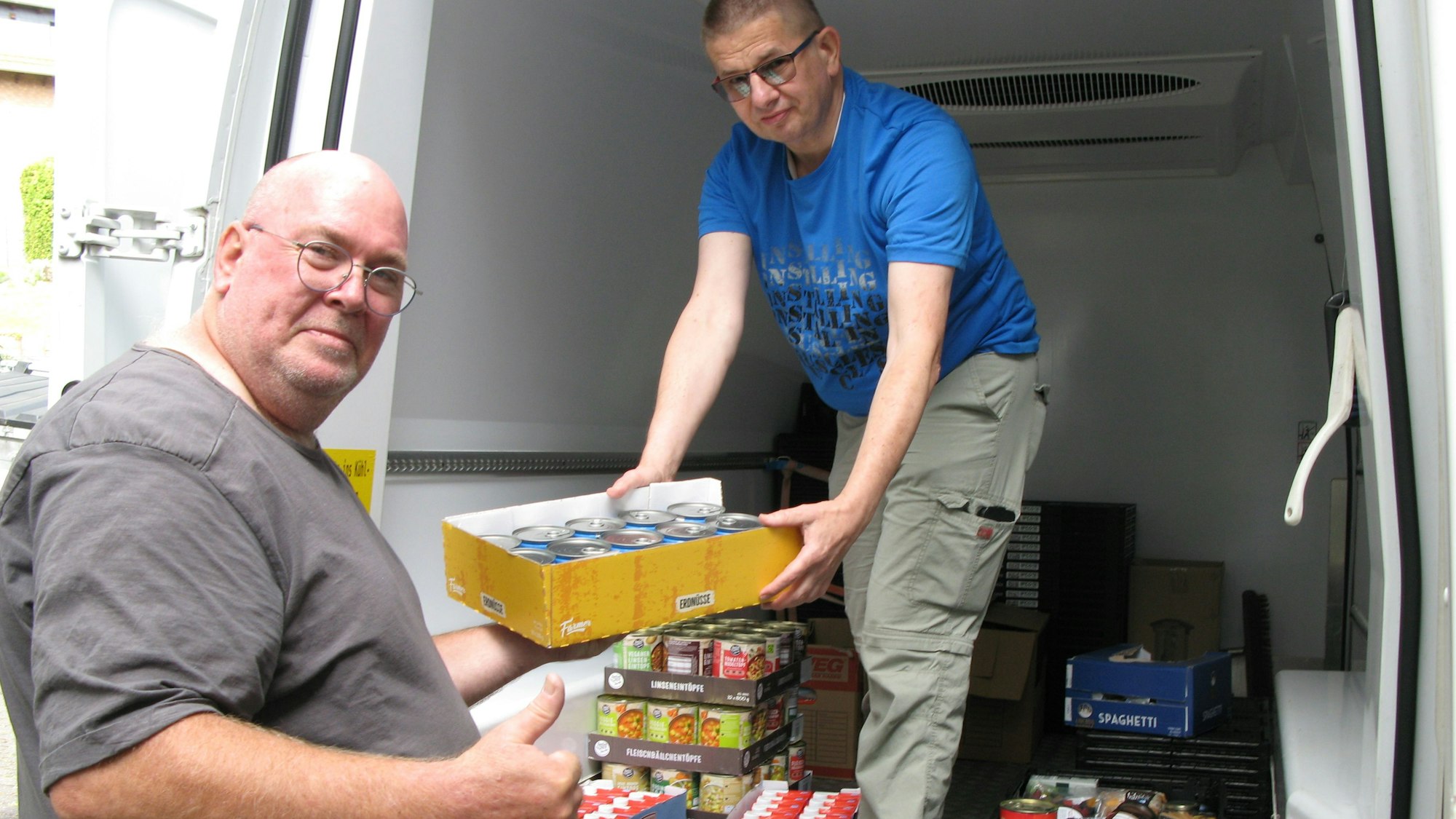 Ein Mann reicht einem anderen Mann, der in einem Transporter steht einen Karton mit gespendeten Lebensmitteln an.