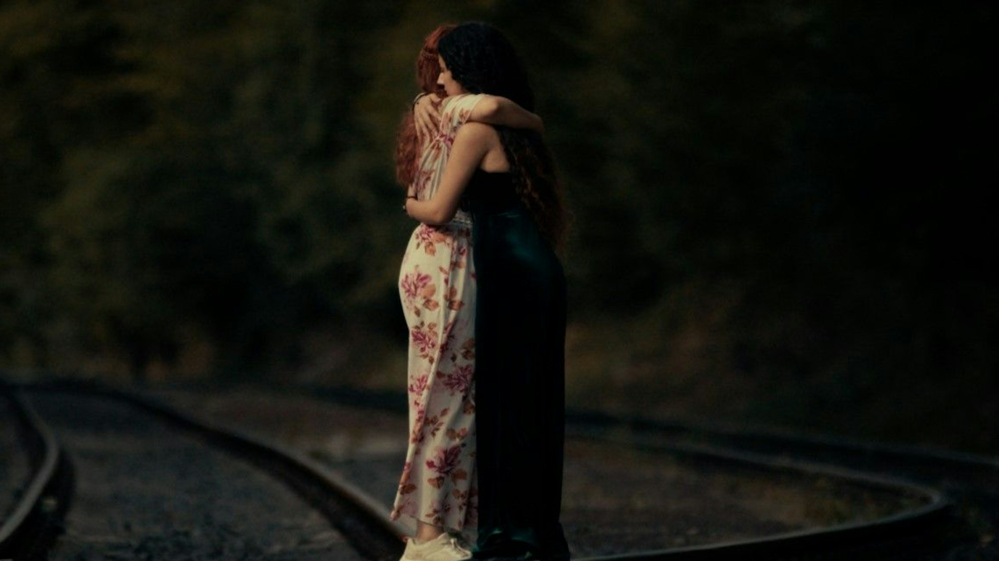 Zwei junge Frauen stehen auf Bahngleisen und umarmen sich.