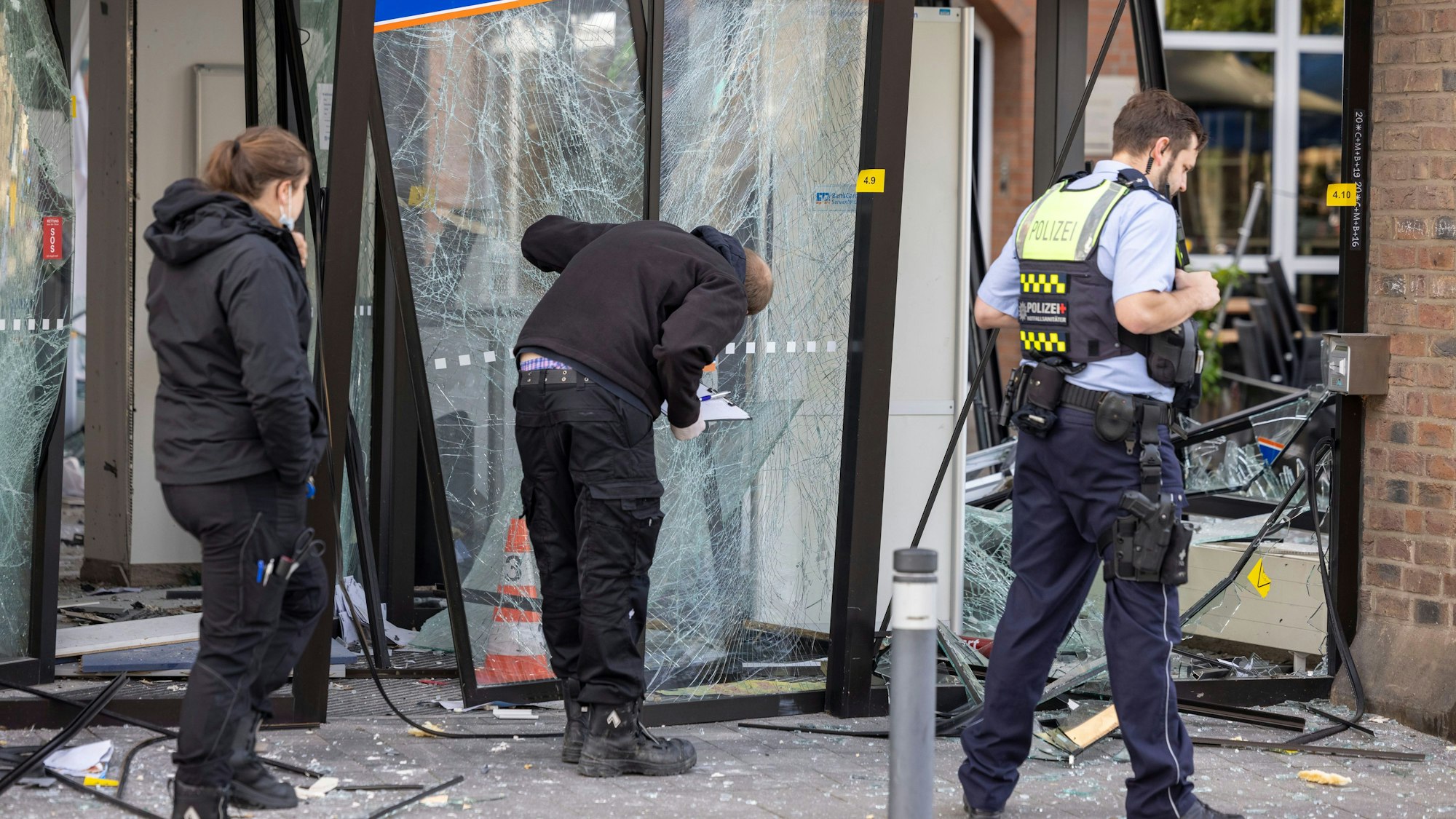 Einsatzkräfte der Polizei untersuchen den Eingang eine Bank, der nach einer Geldautomatensprengung zerstört wurde.