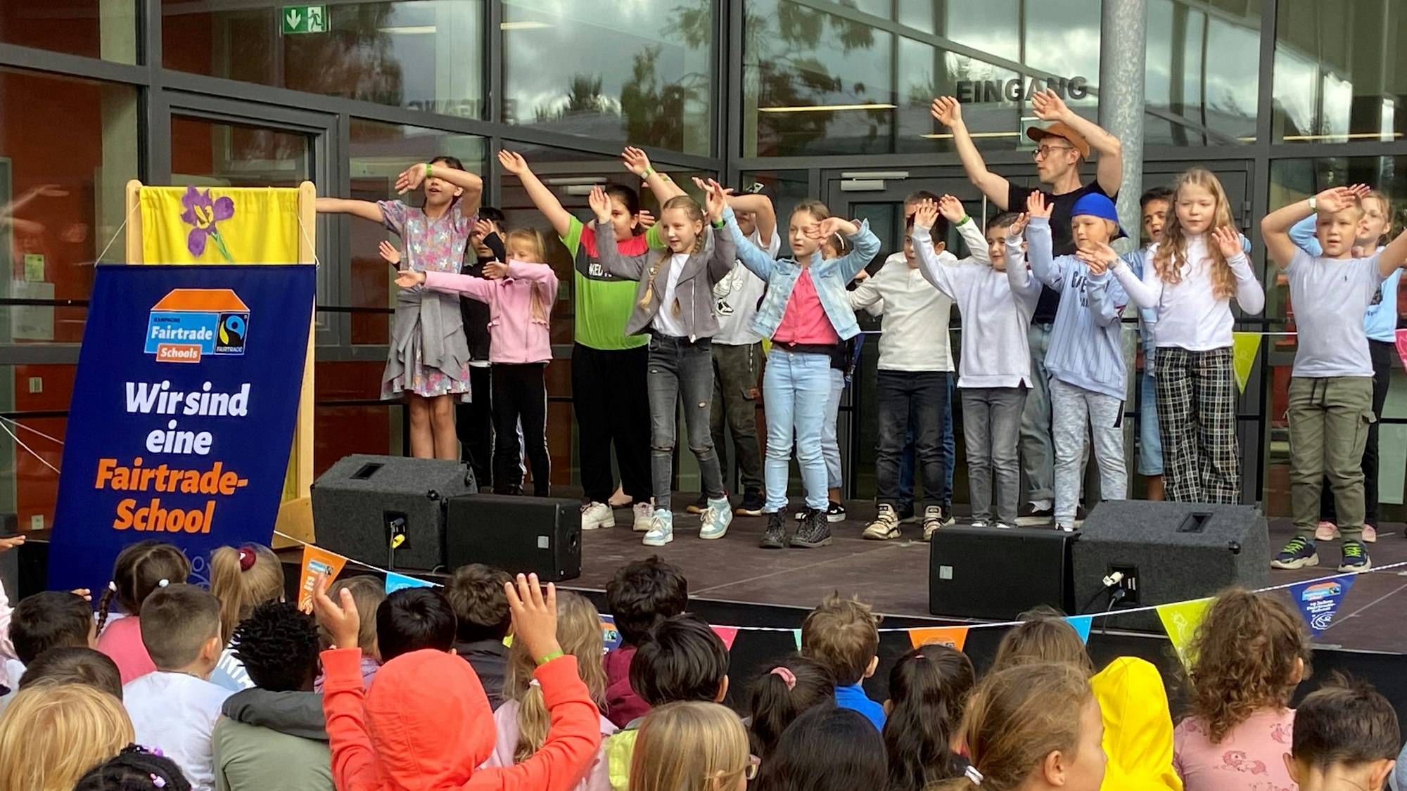 Kinder stehen mit erhobenen Armen auf einer Bühne und singen.