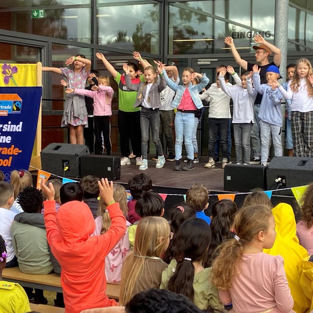 Kinder stehen mit erhobenen Armen auf einer Bühne und singen.