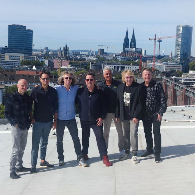 Die sieben Bandmitglieder der Band „"Die Prinzen" “stehen auf dem Dach der Lanxess Arena. Im Hintergrund sieht man das Panorama der Stadt Köln.