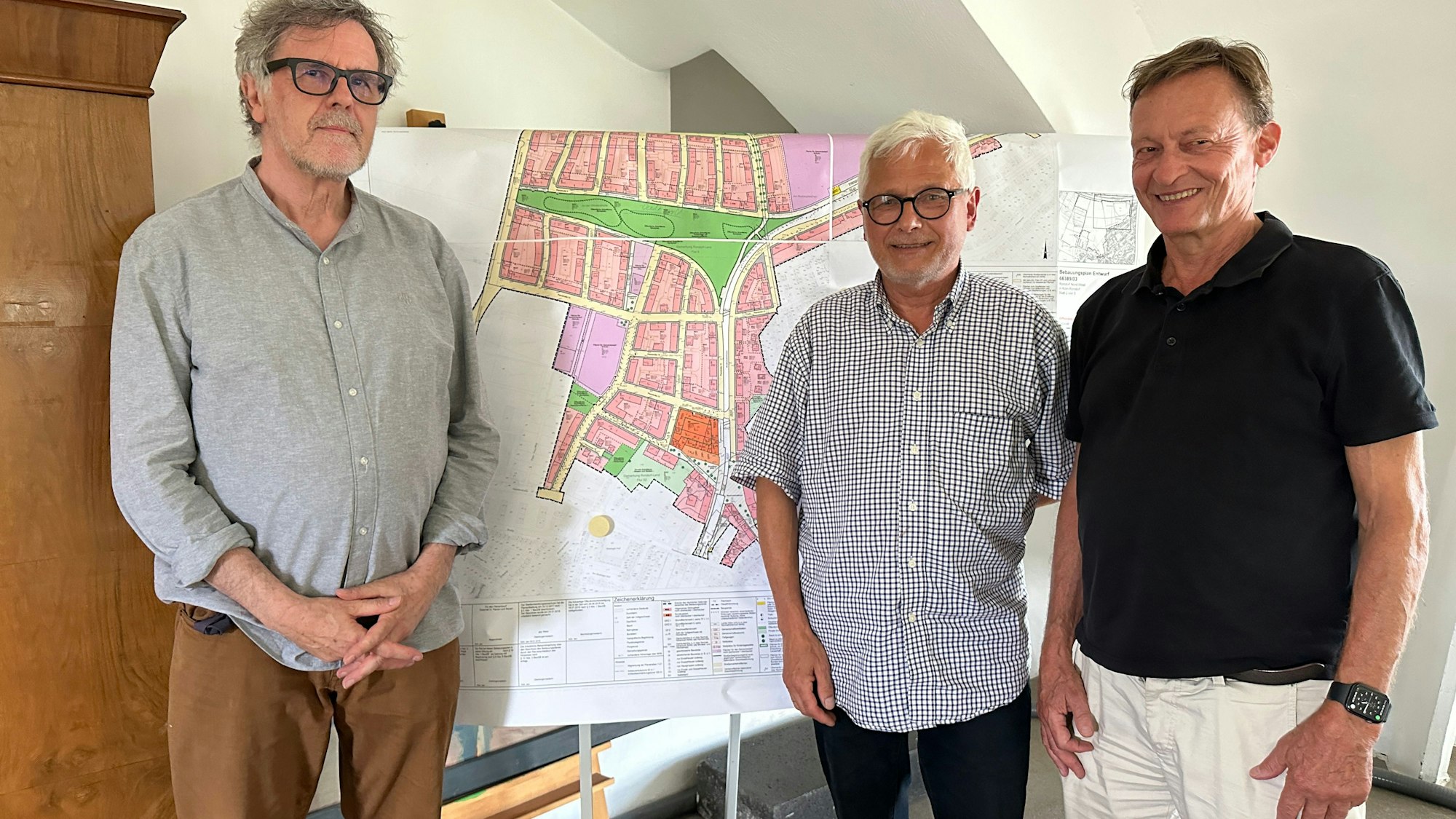 Drei Männer stehen vor einem Aufsteller mit einem Stadtplan.