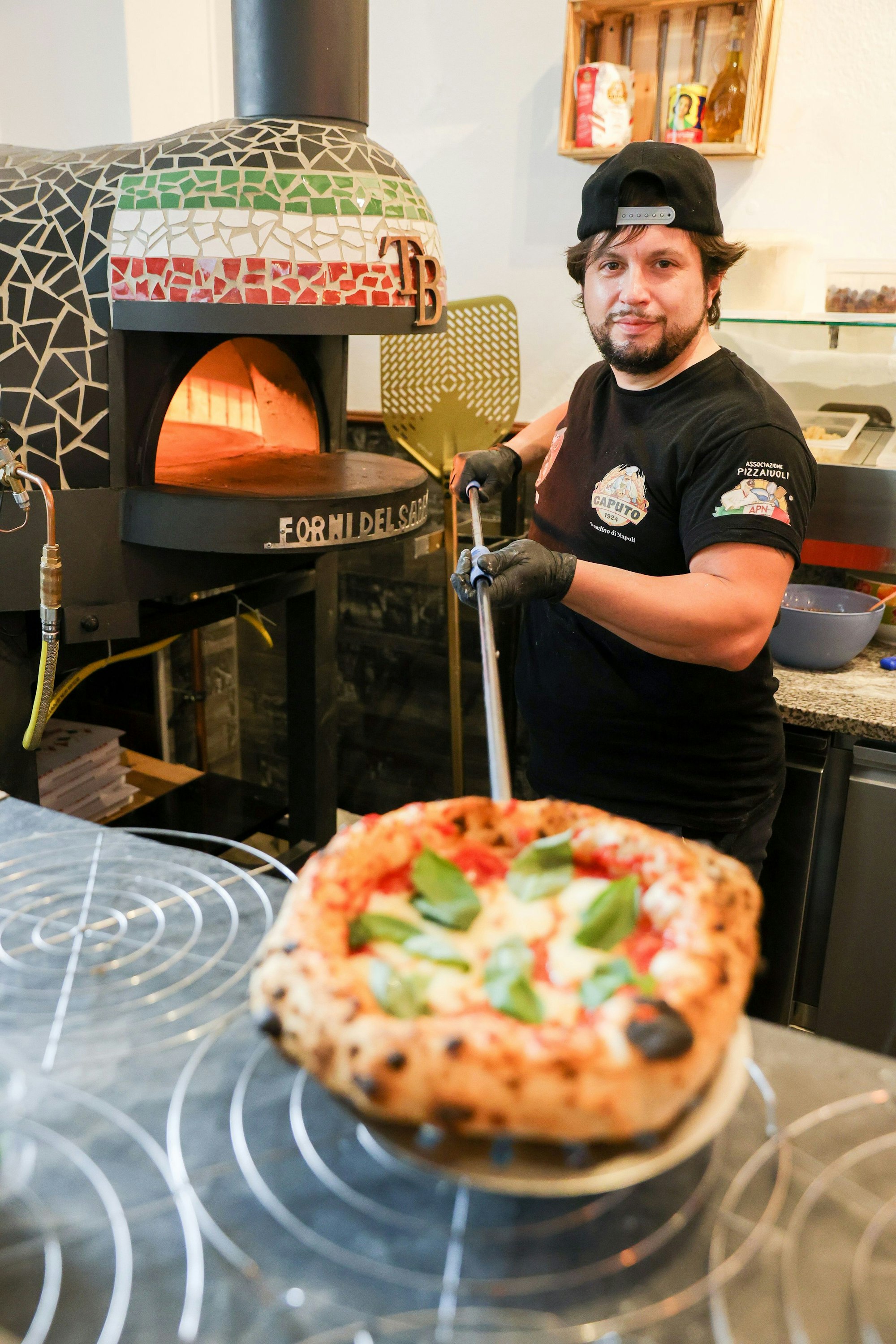 Der Pizzabäcker steht vor dem Ofen und präsentiert seine Pizza.