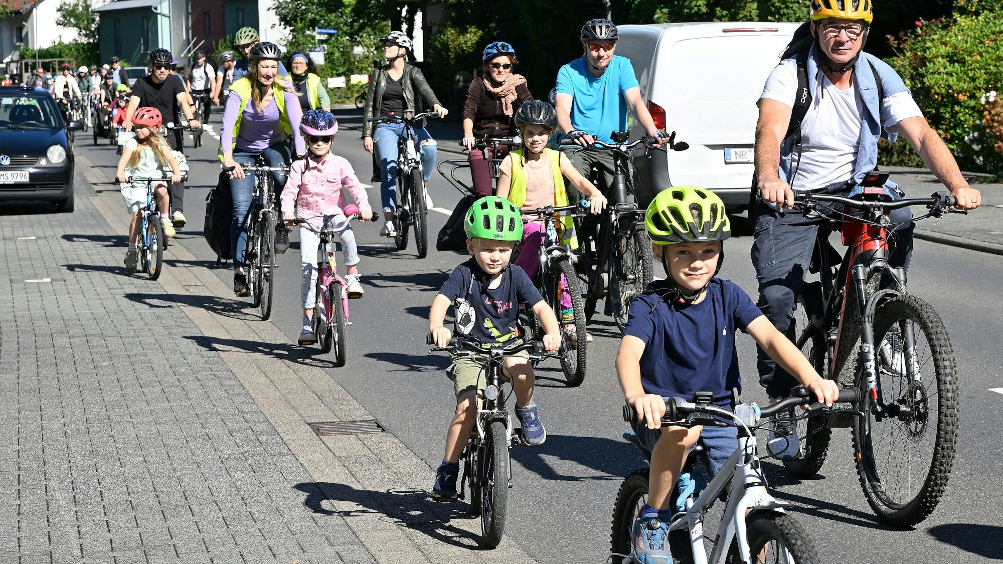 Kinder auf Fahrradhelmen radeln auf der Straße neben Müttern und Vätern.