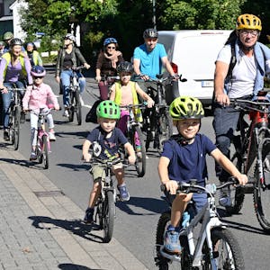 Kinder auf&nbsp; Fahrradhelmen radeln auf der Straße neben Müttern und Vätern.