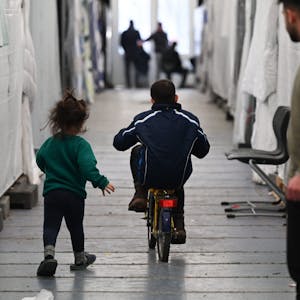 Flüchtlinge in Zelten, Wohncontainern und Turnhallen gehören auch in NRW längst wieder zur Realität. Ein kleiner Junge fährt auf einem Fahrrad zwischen Planen hindurch, ein kleines Mädchen eilt hinter ihm her.