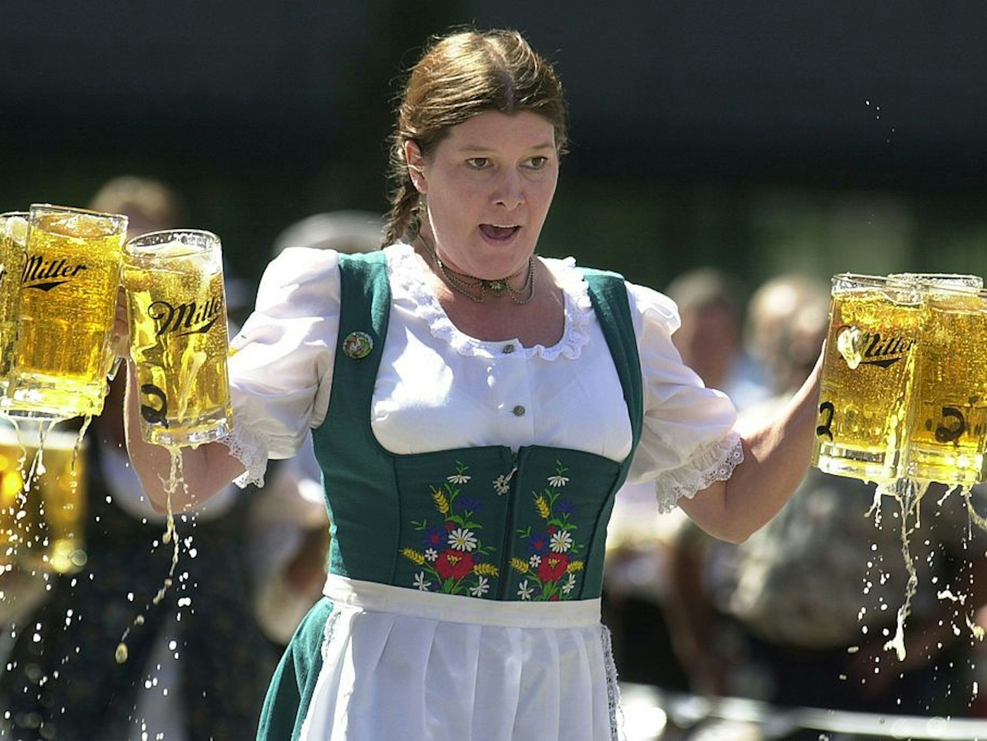 Eine Frau im Dirndl trägt sechs Krüge mit Bier.