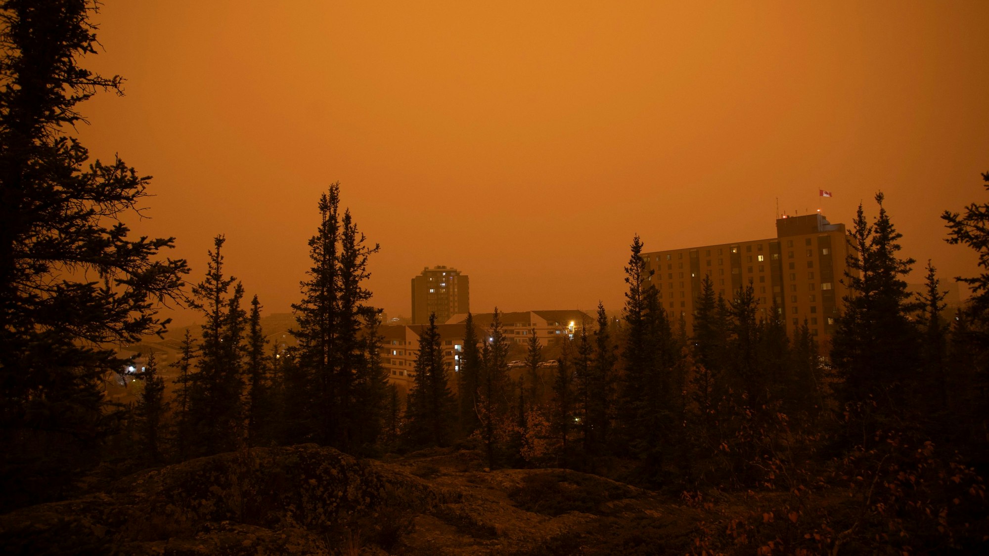 Starker Rauch von Waldbränden im Norden von Alberta und British Columbia zieht über die Stadt Yellow Knife im kanadischen Bundesstaat Northwest Territories hinweg. Die Gebäude und der Wald sind in einen gelben und orangefarbenen Nebel gehüllt.