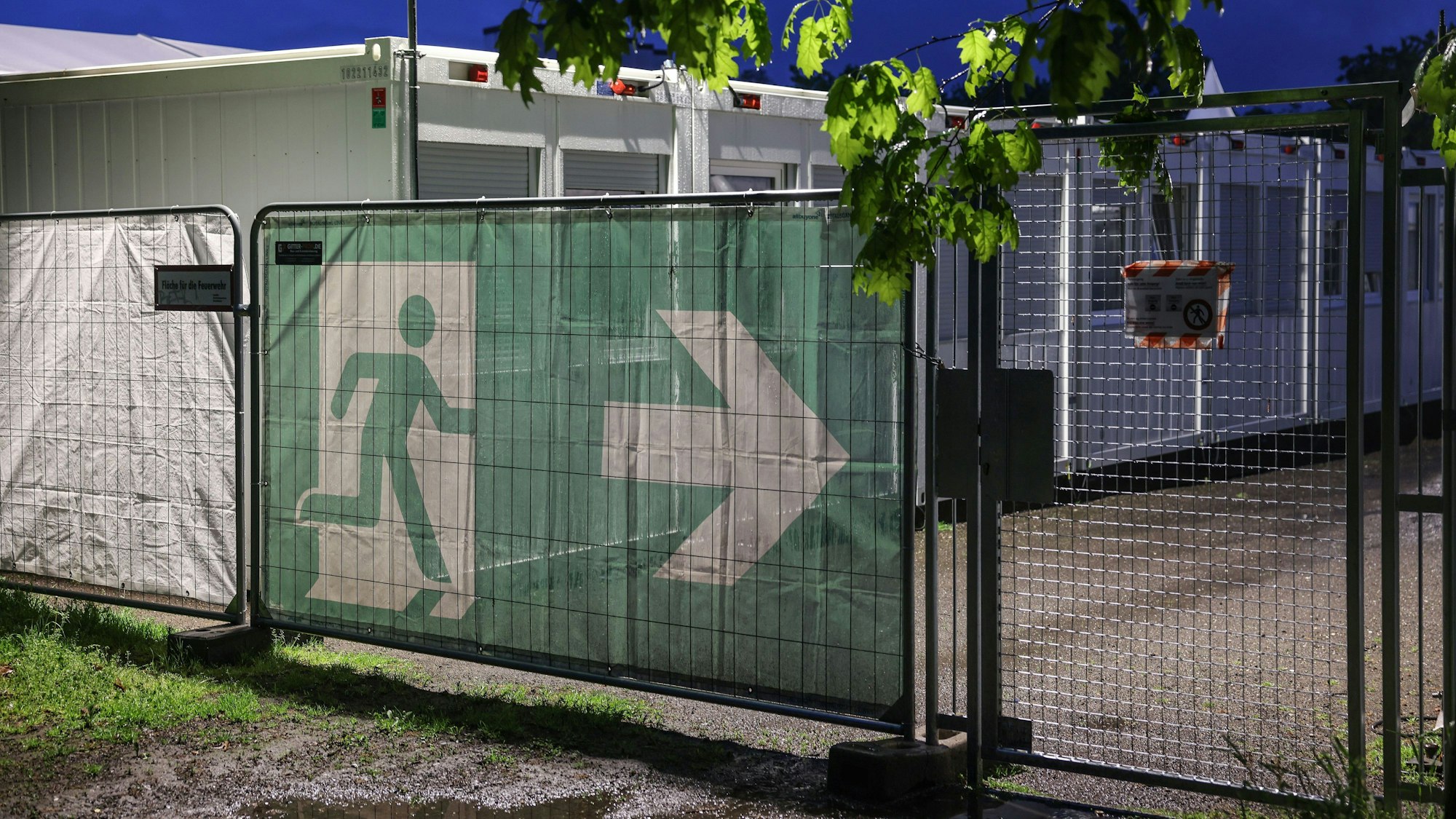 Ein Transparent mit dem Symbol für den Fluchtweg hängt vor Wohncontainer der kommunalen Erstaufnahmeeinrichtung in Köln-Zollstock.