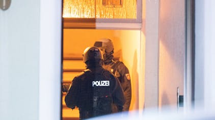 Zwei Polizisten stehen hinter einer Haustür im Treppenhaus.&nbsp;
