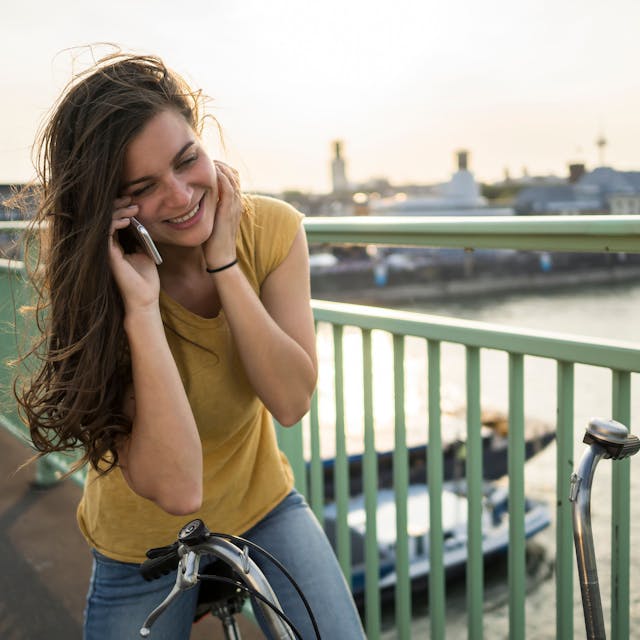 Eine Frau steht auf einer Brücke in Köln auf ihrem stehenden Fahrrad und telefoniert
