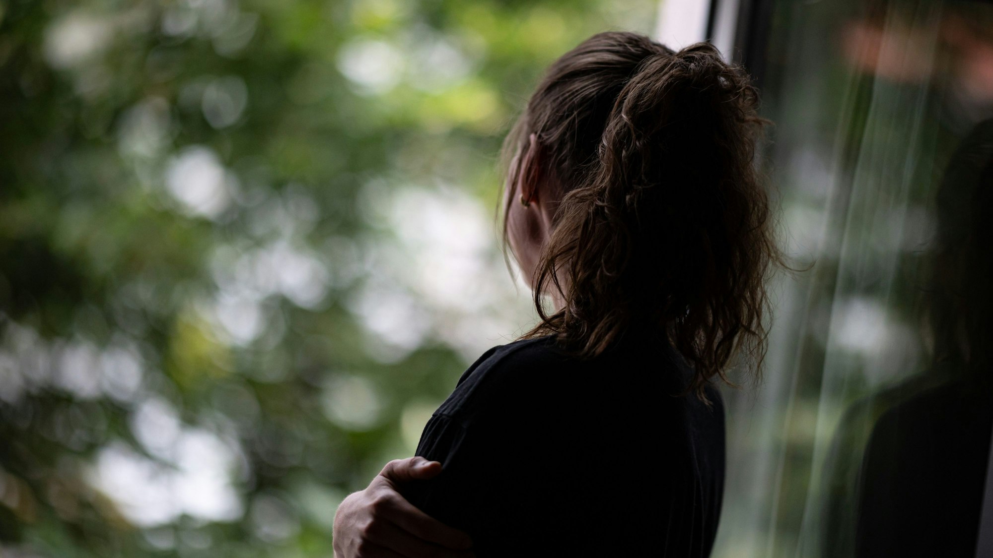 Eine Jugendliche steht gedankenversunken am Fenster.