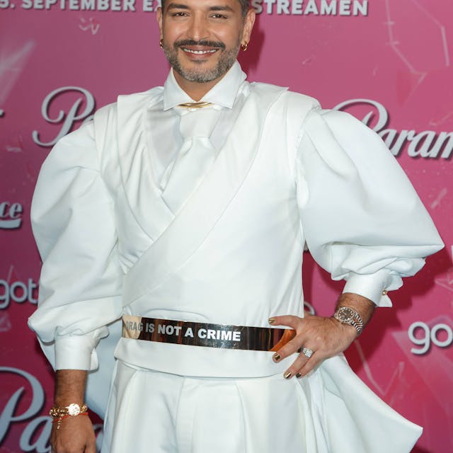 Gianni Jovanovic bei der Premiere der Show „Drag Race Germany“, die beim Streamingdienst Paramount+ zu sehen ist. Er trägt ein weißes Hemd, eine weiße Krawatte und lächelt in die Kamera.