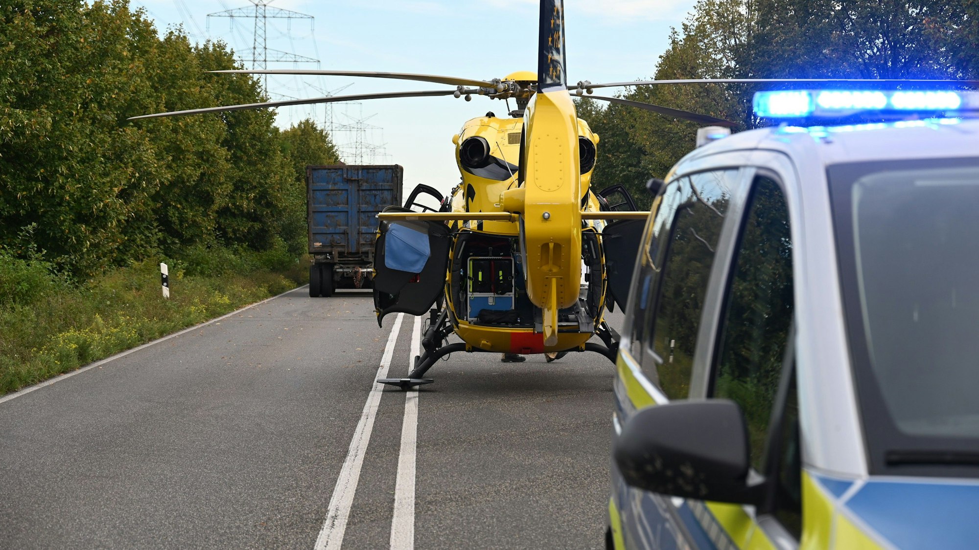 Auf dem Foto sind ein gelber Rettungshubschrauber, ein Einsatzfahrzeug der Polizei und im Hintergrund ein Lkw auf der B 59 zu sehen.