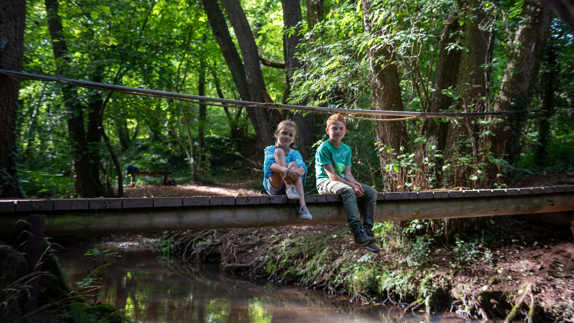 Ein Mädchen und ein Junge sitzen auf einer kleinen Brücke mitten im Wald.