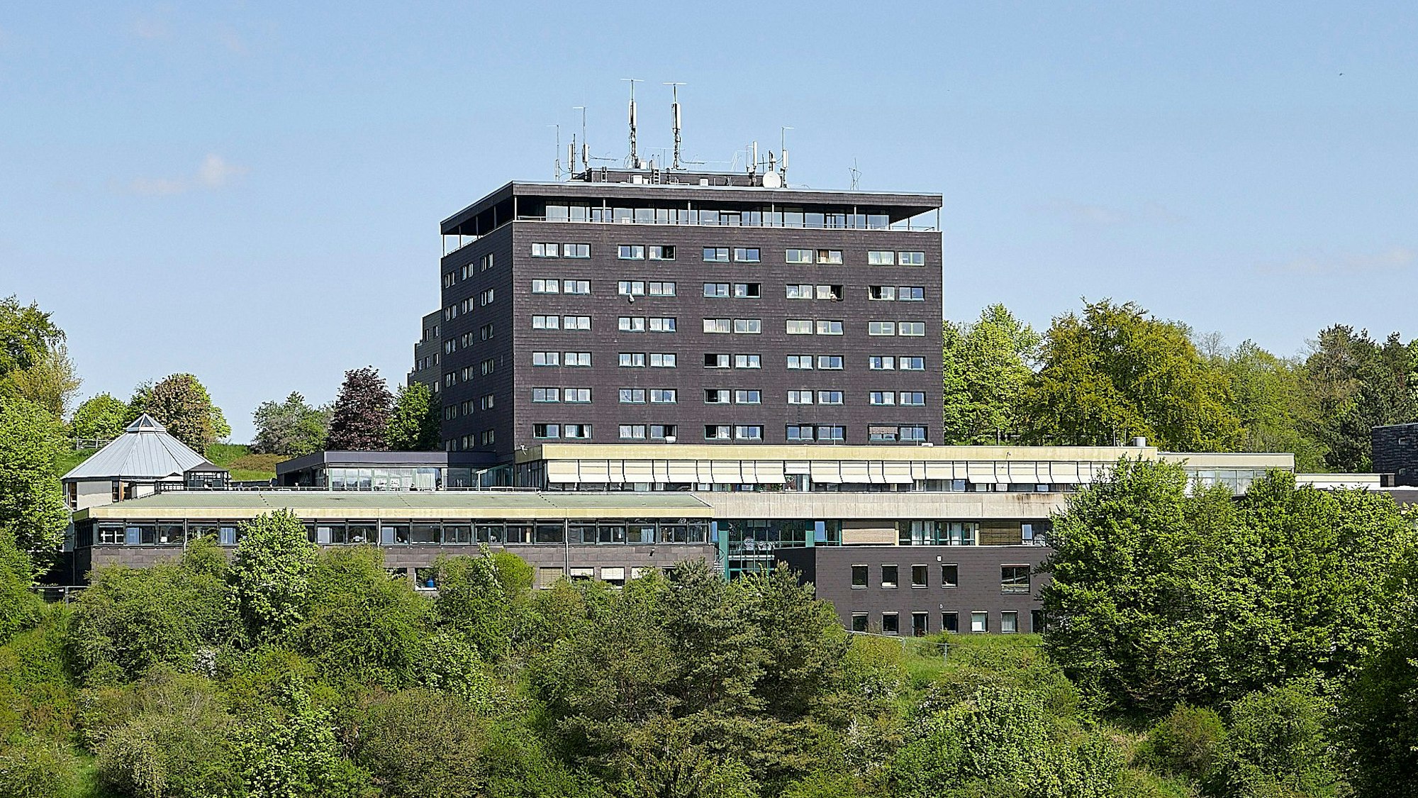 Umgeben von grünen Bäumen und Sträuchern ist der mehrstöckige Gebäudekomplex der ehemaligen Eifelhöhen-Klinik.