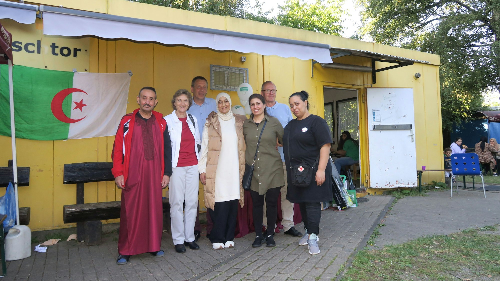 Rolf Blandow und Thomas Bischofs mit Claudia Greven-Thümer sowie Ali Elmakhfi, Naziha Almakhti, Leila Sulayiman und Hanan Almahi stehen vor einem gelben Container.
