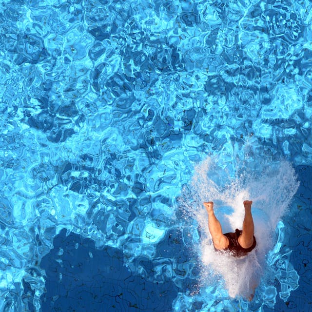 Ein Badegast springt kopfüber ins schillernd blaue Schwimmbecken.&nbsp;