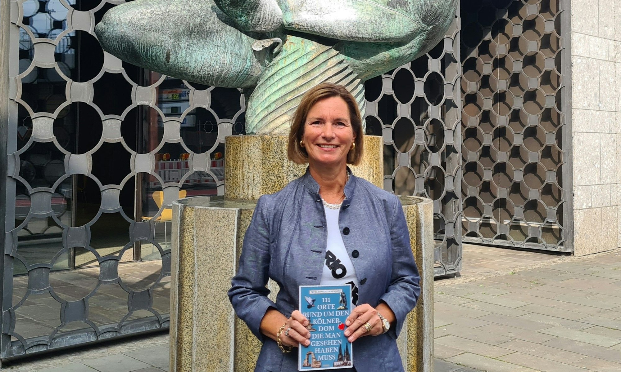 Autorin Petra Sophia Zimmermann präsentiert ihr neues Buch vor dem Baptisterium am Kölner Dom.