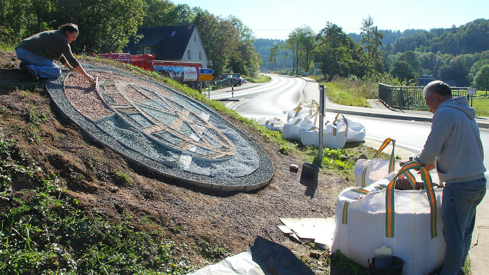 Ein Mühlrad aus farbigem Splitt ist auf der Insel des Kreisverkehrs in Ahrhütte zu sehen.