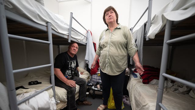 Halina und Oleg aus der Ukraine sitzen und stehen in der Notunterkunft für Geflüchtete am ehemaligen Flughafen Tegel zwischen ihren Betten in einem 12-Bett-Zimmer.&nbsp;