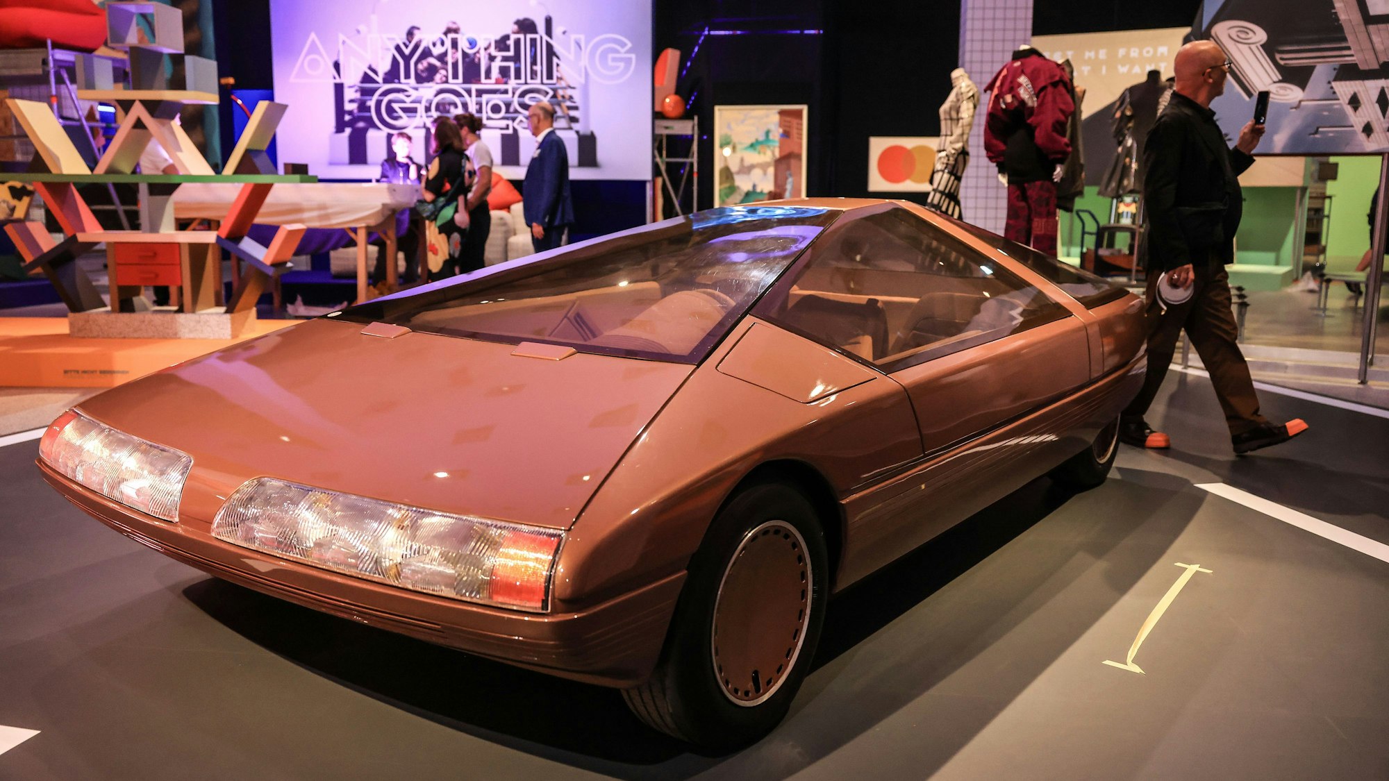 Das Konzeptfahrzeug "Citroen Karin" aus dem Jahr 1980 steht in der Bundeskunsthalle. Es ist rötlich und geometrisch-schnittig. Im Hintergrund weitere bunte Kunstwerke und Besucher.