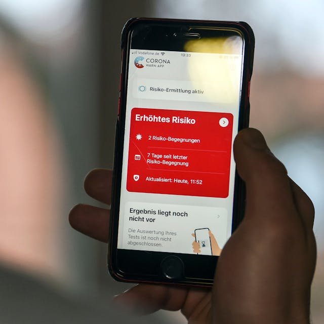 Ein Mann hält ein Smartphone in der Hand, auf dem die Corona-App in einem roten Feld „Erhöhtes Risiko“ anzeigt.&nbsp;