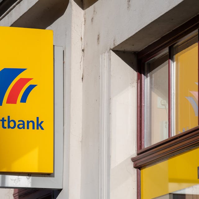 Ein Schild mit dem Logo der Postbank ist an der Fassade einer Bankfiliale angebracht. (Symbolbild)