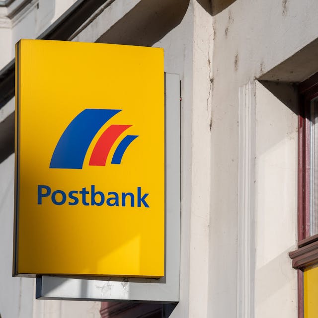 Ein Schild mit dem Logo der Postbank ist an der Fassade einer Bankfiliale angebracht. (Symbolbild)