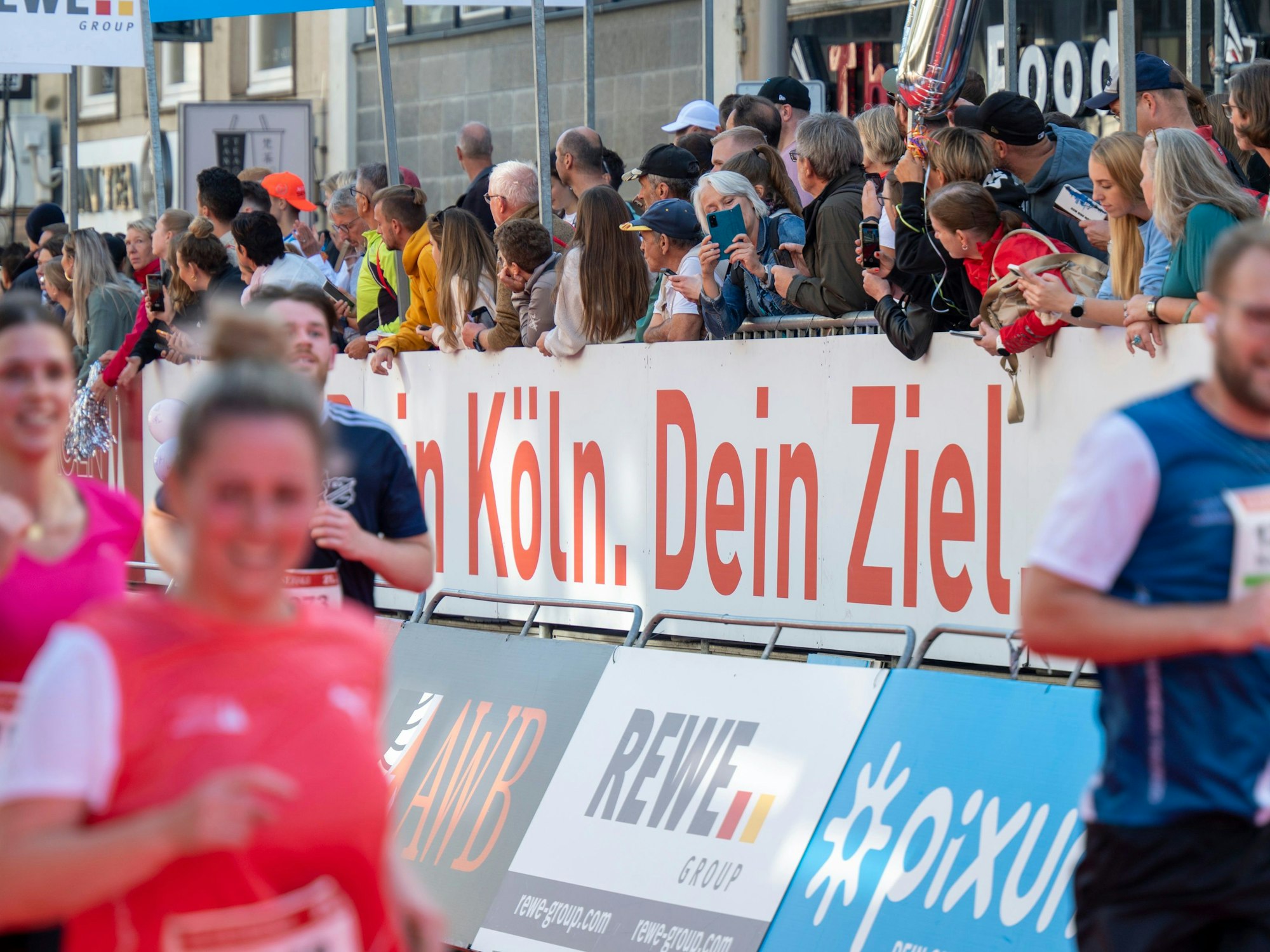 Menschen verdecken einen Teil eines Plakates, sodass dort nur noch zu lesen ist „Köln.Dein Ziel“.