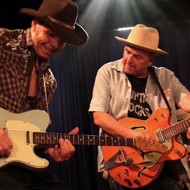 Zwei Musiker von Hillbilly Deluxe mit Gitarre und Cowboy-Hüten.