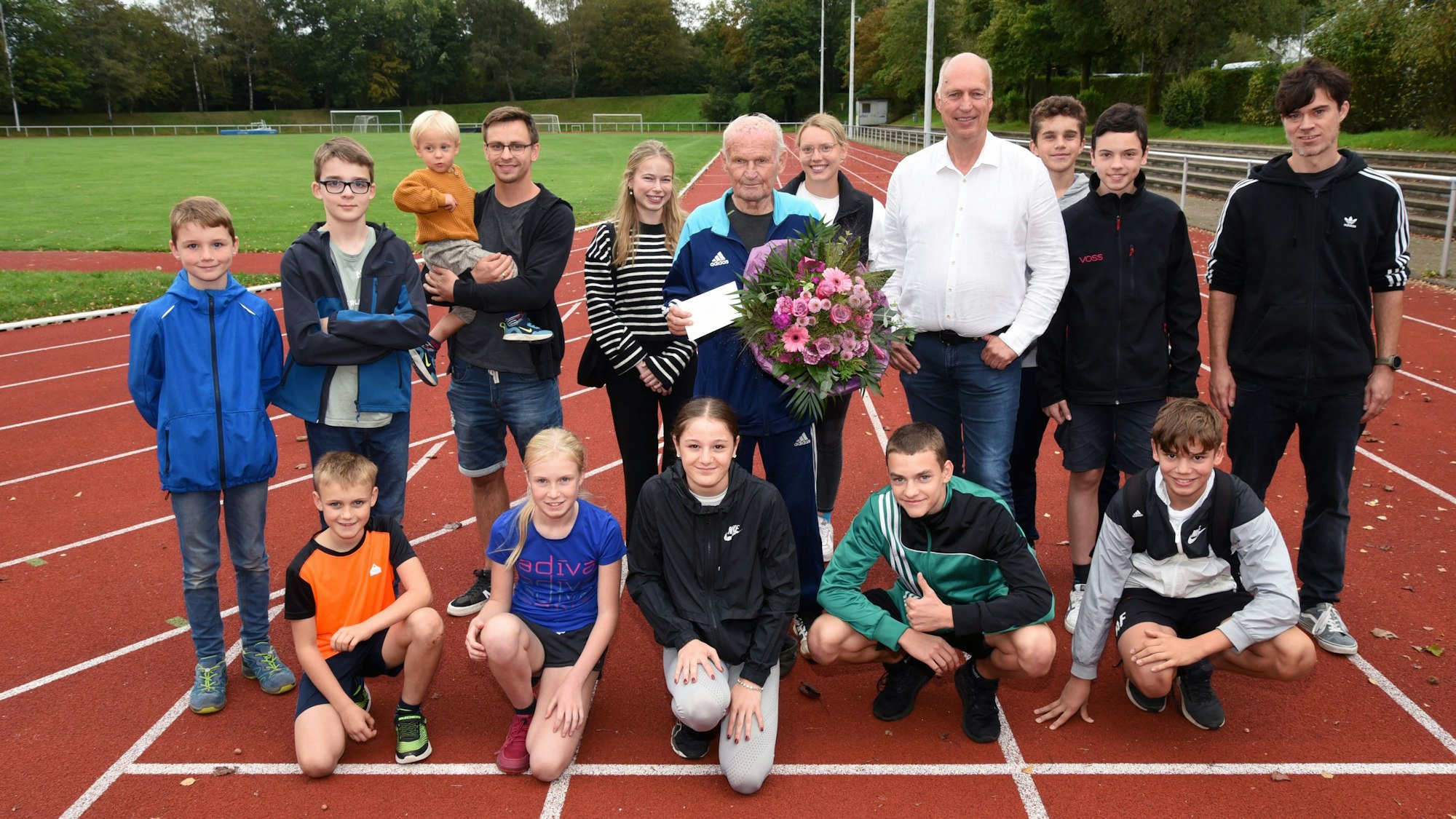 Kinder und weitere Sportler auf einer Laufbahn mit Oswald Pankalla, der einen Blumenstrauß in der Hand hält.