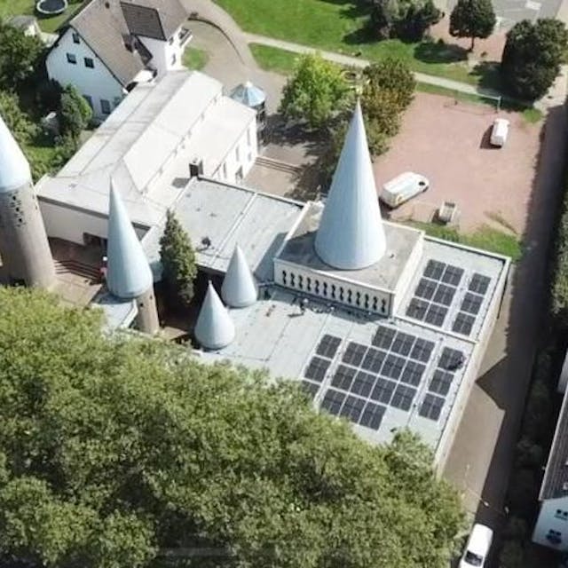 Das Foto ist aus der Luft aufgenommen: Man sieht die Solarmodule in Schwarz auf einem Teil des Kirchendachs. Sie sind platziert vor den fünf unterschiedlich großen drei Kirchtürmen.