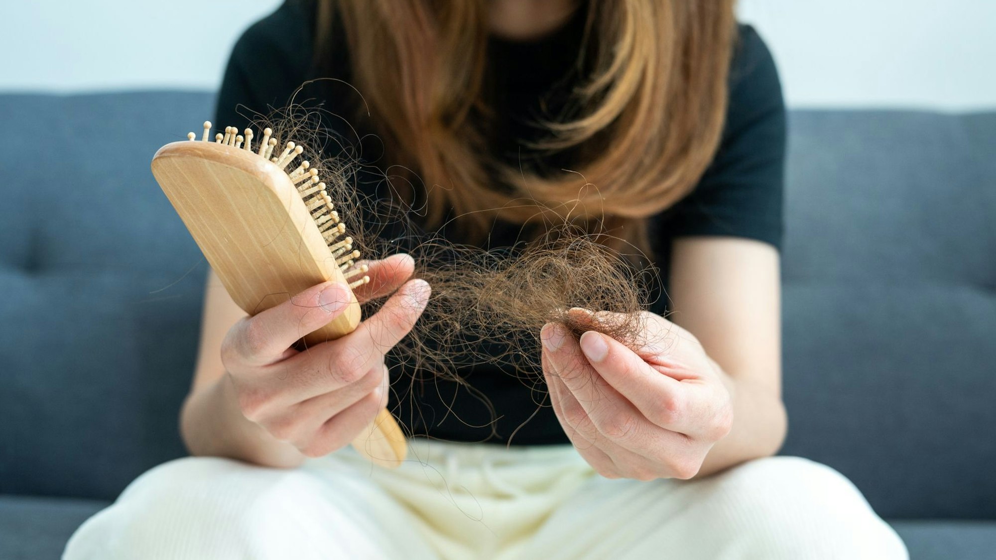 Eine Frau zieht verlorene Haare aus einer Haarbürste.