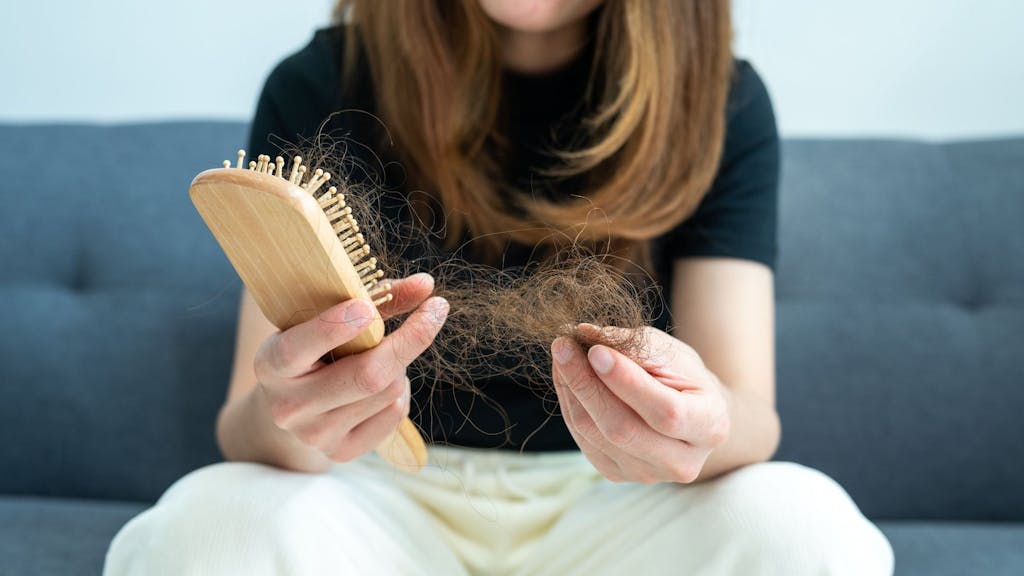 Eine Frau zieht verlorene Haare aus einer Haarbürste.